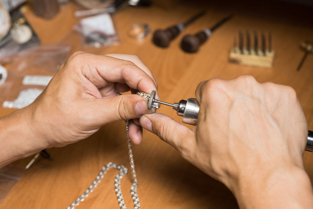 Man working on jewelry repair of a silver bracelet on desk.
