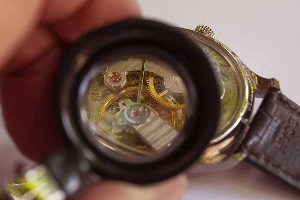 Using a magnifying glass to see the inside of a watch. Watchmaker in process of watch engraving.
